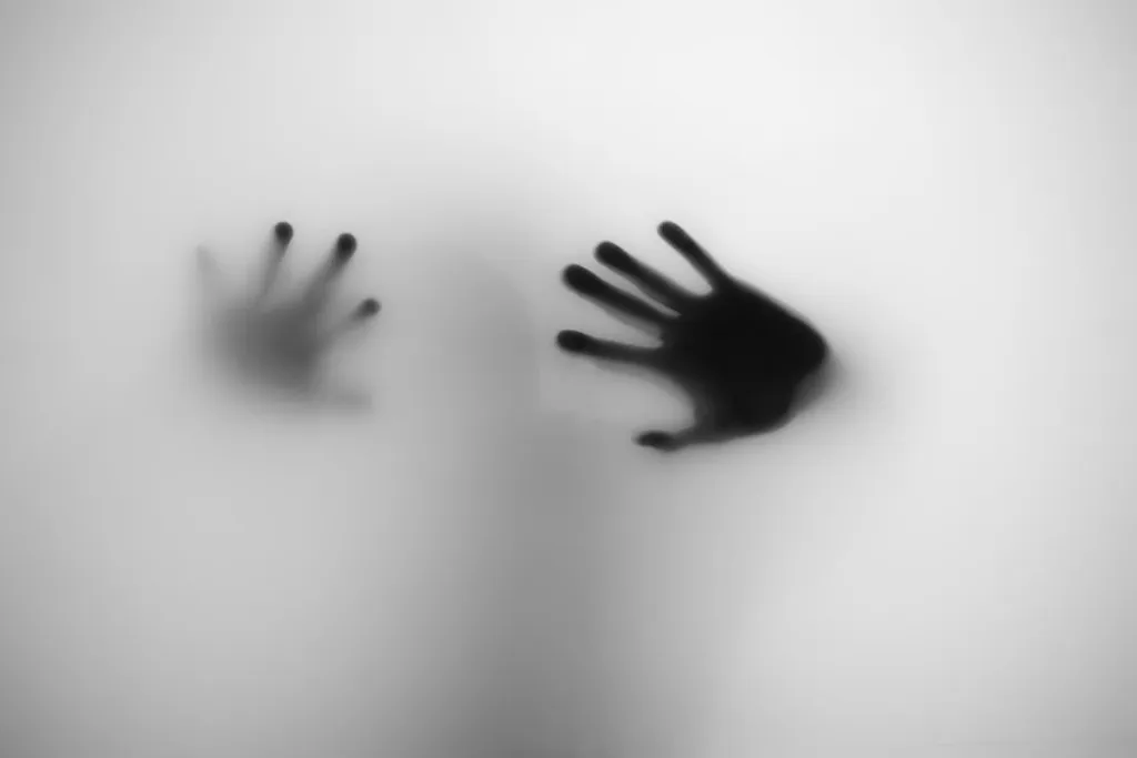 Two hands pressed to frosted glass with fingers spread — one dark and close, the other faint behind it.