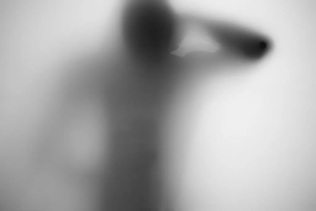 A softened figure leaning back with one arm stretched upward against frosted glass.